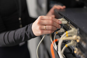 Woman IT technician connects network cables to server rack in data center for maintenance