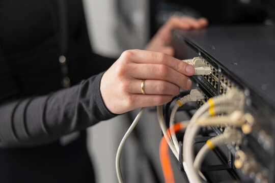 Woman IT technician connects network cables to server rack in data center for maintenance