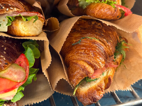 Croissant sandwiches with lettuce, tomato, and cheese in paper bags. Fresh breakfast, street food, and quick cafe meal concept. Close-up