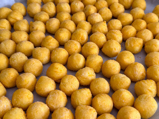 Rows of small fried potato balls on parchment paper close-up. Homemade snack, food texture, and simple culinary composition pattern.