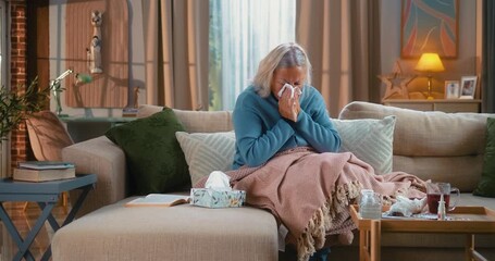 Ill woman with flu sitting on a couch at home, covered with a blanket, sneezing and coughing while using tissues. Indoor winter scene showing sickness, fatigue, and recovery. - Powered by Adobe