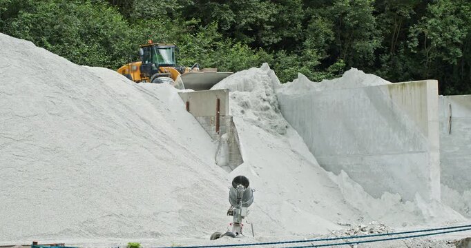 Wheel loader dumping aggregate into concrete storage bay, pouring white gravel onto stockpile at quarry, heavy construction materials handling