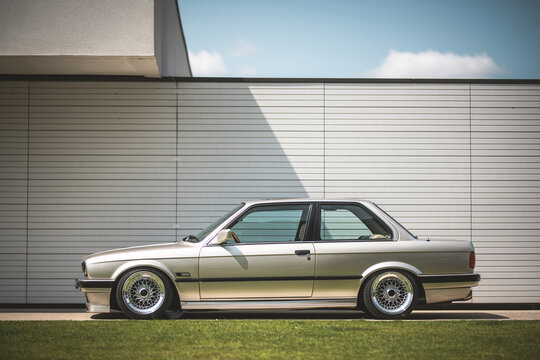 Classic silver coupe parked in front of a modern building on a sunny day