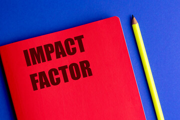 Words impact factor printed on red notebook with yellow pencil on blue background
