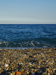 A balanced coastal scene near Taormina, Sicily, featuring equal stripes of gray rocky beach, darker blue sea, and clear sky. Peaceful and scenic, ideal for travel and landscape use.