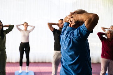 Instructor leading a diverse group of people during a fitness training session with stretching exercises on mats in a bright wellness center