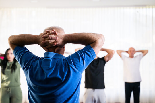 Instructor leading a diverse group of people during a fitness training session with stretching exercises on mats in a bright wellness center