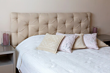 Bedroom interior. Elegant bedroom featuring beige headboard adorned with decorative pillows, complemented by soft white bedspread, creating serene and inviting atmosphere for relaxation and comfort