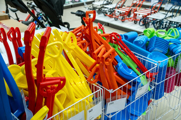 A wide assortment of vibrant plastic snow shovels for children neatly displayed in a store. The image showcases a variety of colors including red, yellow, blue, and green.