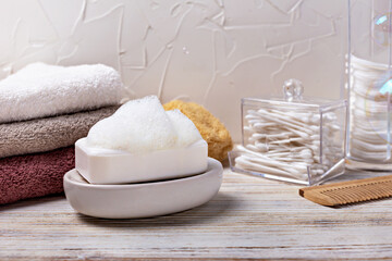 Health and hygiene. Soap bar with foam placed on dish, surrounded by neatly stacked towels and cotton swabs, creating calming atmosphere in bathroom, emphasizing cleanliness and relaxation