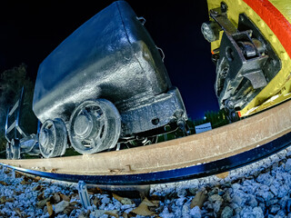 Nocny widok z niskiej perspektywy na wagony kopalniane na torach,  dwa zabytkowe wagony kopalniane na zakrzywionych torach kolejowych nocą. Tory ułożone są na białym żwirze © PIOTR D