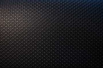 Macro photo of a modern black textured surface. The embossed geometric pattern creates a dark, abstract background with a premium, technical feel. Selective focus adds depth.