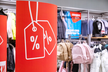 Fototapeta premium Red sale banner with discount symbols prominently displayed in a clothing retail store. Background features various apparel showcasing the lively shopping environment during a sale event.
