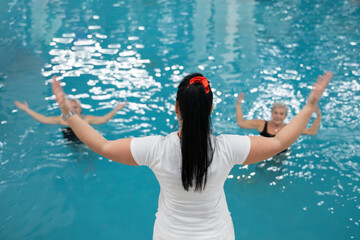 Instructor leading aquatic fitness training for group senior women in a swimming pool. Concept of health, exercise, wellness, water therapy, and active aging lifestyle