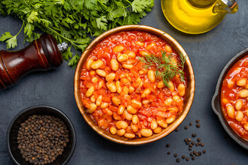 Baked bean dish in wooden bowl on black background.
