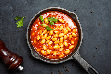 Baked bean dish in cast iron pan on black background. 