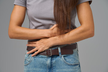 Close-up of woman s hands clutching stomach in pain, studio shot on neutral grey