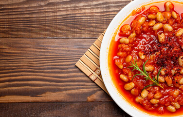 Baked bean dish in white plate on wooden background.