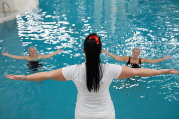 Instructor leading aquatic fitness training for two senior women in a swimming pool. Concept of health, exercise, wellness, water therapy, and active aging lifestyle.
