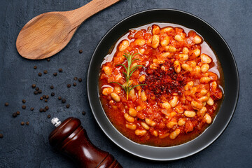 Baked bean dish in  black plate  on black background.