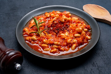 Baked bean dish in  black plate  on black background.