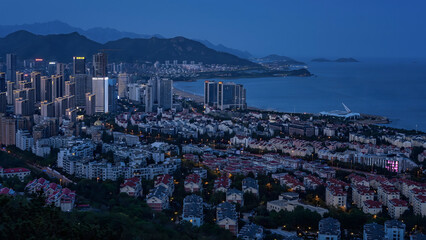 Qingdao City Skyline at Dusk with Coastal Mountains and Illuminated Buildings