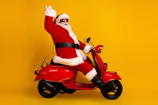 Santa on a bright red scooter waves hello as he rides against a bold yellow background for a festive Christmas moment perfect for holiday