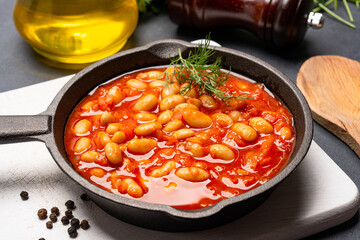 Baked bean dish in cast iron pan on black background. 