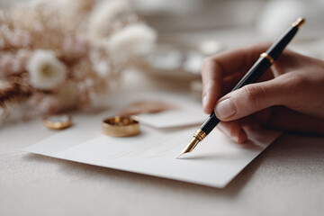 Elegant hand writing on paper with a fountain pen. Wedding rings nearby. Symbolizes love, commitment, vows, and a new beginning. Perfect for wedding stationery or heartfelt messages.