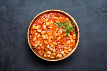 Baked bean dish in wooden bowl on black background. 