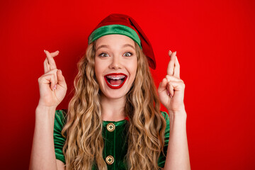 Festive young woman in a green elf costume with crossed fingers expressing holiday excitement...