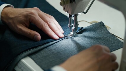 Close-up of a tailor sewing dark blue fabric on a professional machine, highlighting craftsmanship and detail in garment creation