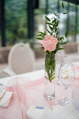 Elegant table setting with a single pink rose in a clear glass vase surrounded by delicate pink fabric and shimmering glassware creating a romantic atmosphere for a special event celebration