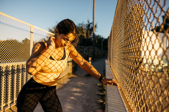 Woman runner stretching by fence during sunset workout