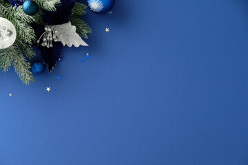Christmas corner composition with pine, silver and blue ornaments on blue background, decorated...