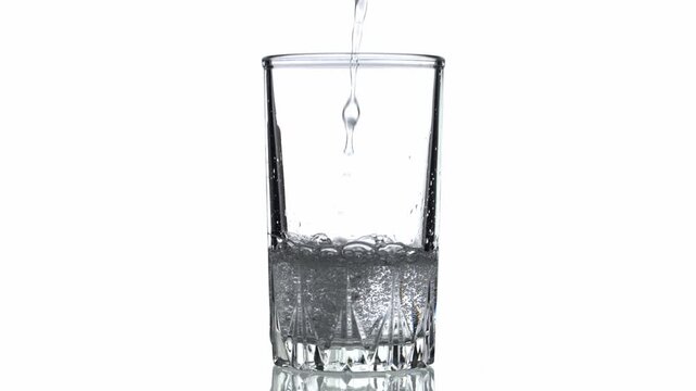 A glass of water is being poured into it. The water is clear and the glass is half full