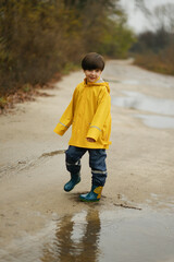 Happy child in a yellow raincoat jumping in puddles on a rainy autumn day in the park.