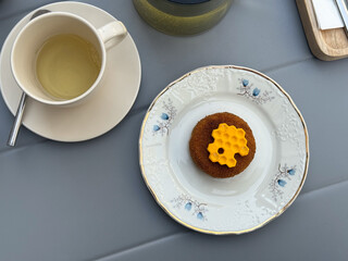 Cup of tea and dessert on elegant porcelain plate. Cozy outdoor cafe breakfast, minimal lifestyle, and slow living concept.