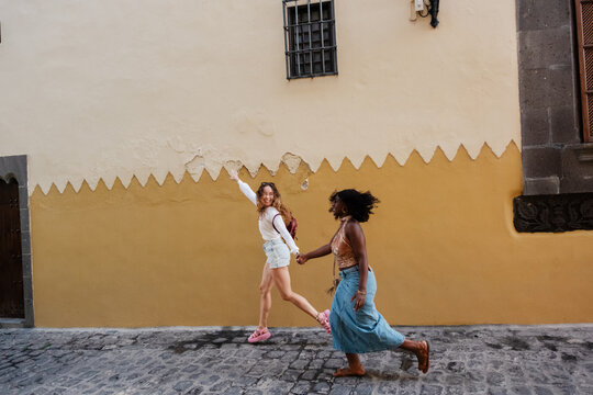 Two diverse women friends running holding hands on holiday