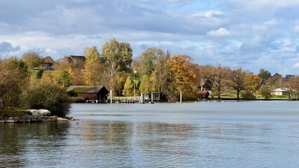 On the shore of Lake Zug in Buonas, Risch, a beautiful autumn day unfolds with crisp air, gentle waves, and a blue sky scattered with soft clouds.