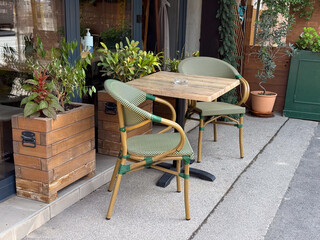 Wooden cafe table with green chairs and potted plants. Urban outdoor dining, cozy atmosphere, and small street cafe lifestyle.