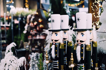 Wooden nutcracker soldier decorations in a Christmas market surrounded by lights, trees, and...