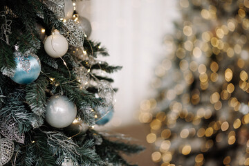 Close-up of Christmas tree with blue and silver baubles, glitter leaves and warm lights with copy space. Blurred festive background. Concept of winter holiday, celebration, decoration, greeting card.