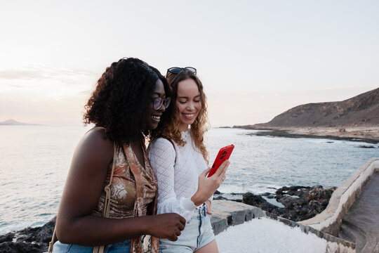 Diverse women friends laughing at smartphone on vacation