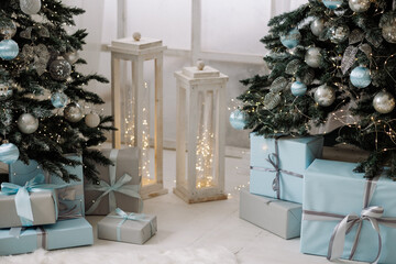 Decorated Christmas trees with blue and silver baubles and wrapped gifts on white wooden floor. Concept of winter holidays, celebration, cozy home interior.