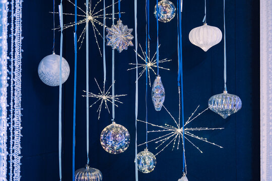 Hanging crystal and glass Christmas ornaments with starburst lights on a dark blue backdrop. Iridescent ornaments, celestial holiday trend, crystal starburst lights, cosmic Christmas