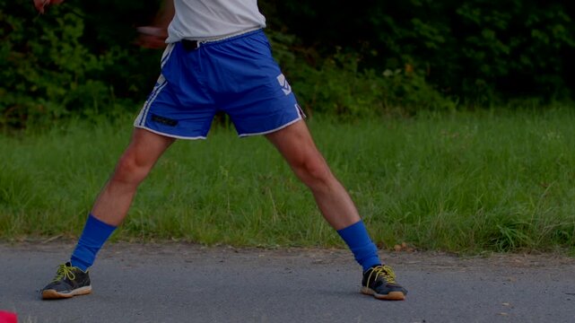 white male outdoor agility session wide lateral jumps legs spread dynamic motion blue socks supportive shoes roadside