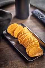 Crispy potato chips on plate on wooden table.