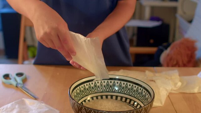 hands prepping rice with plastic wrapper over ceramic bowl, fingers tearing liner and smoothing sticky grains into