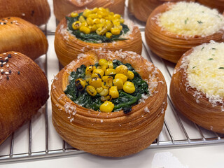 Danish pastry with spinach and corn filling on bakery tray. Gourmet bakery assortment, creative food styling and modern cafe display.